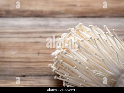 Enoki Pilze auf einem hölzernen Hintergrund platziert. Nahaufnahme, Bild von Pilzen. Stockfoto