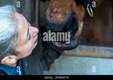 Eine reife Reiterin verbringt die letzten kostbaren Stunden, bevor ein Pferd aufgrund von schlechtem Gesundheitszustand und Alter abgesetzt wird. Stockfoto