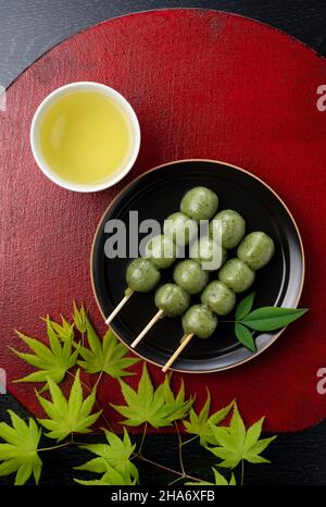 Grasknödel und grüner Tee auf einem roten japanischen Tablett. Japanische Knödel. Blick von direkt oben. Stockfoto