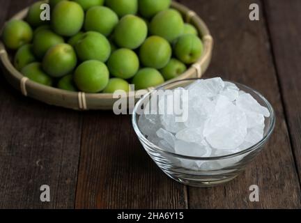 Unreife Ume-Frucht und Steinzucker auf einem hölzernen Hintergrund. Vorbereitung auf die Herstellung von japanischem Pflaumenwein Stockfoto