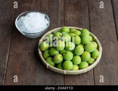 Unreife Ume-Frucht und Steinzucker auf einem hölzernen Hintergrund. Vorbereitung auf die Herstellung von japanischem Pflaumenwein Stockfoto