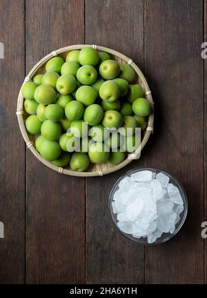 Unreife Ume-Frucht und Steinzucker auf einem hölzernen Hintergrund. Vorbereitung auf die Herstellung von japanischem Pflaumenwein Stockfoto