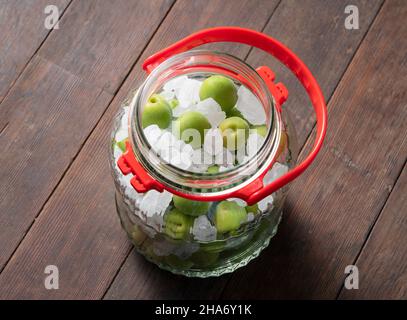 Unreife Ume-Frucht und Steinzucker auf einem hölzernen Hintergrund.Herstellung traditioneller japanischer grüner Pflaumenwein Stockfoto