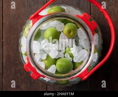 Unreife Ume-Frucht und Steinzucker auf einem hölzernen Hintergrund.Herstellung traditioneller japanischer grüner Pflaumenwein Stockfoto