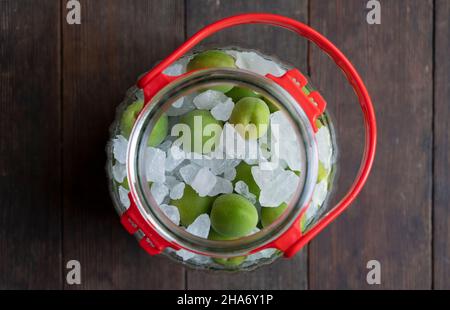 Unreife Ume-Frucht und Steinzucker auf einem hölzernen Hintergrund.Herstellung traditioneller japanischer grüner Pflaumenwein Stockfoto