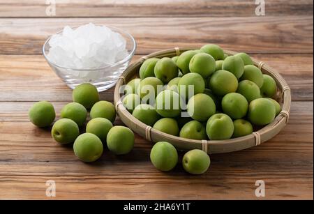 Unreife Ume-Frucht und Steinzucker auf einem hölzernen Hintergrund. Vorbereitung auf die Herstellung von japanischem Pflaumenwein Stockfoto