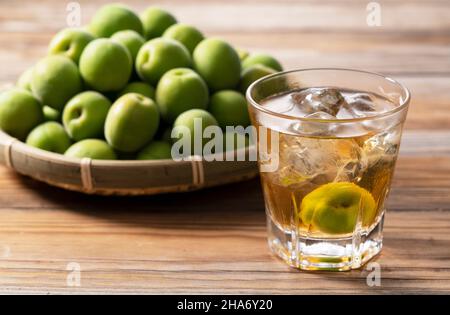 Japanischer Pflaumenwein und unreife Pflaumen auf einem Holzhintergrund. Stockfoto