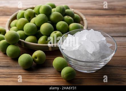 Unreife Ume-Frucht und Steinzucker auf einem hölzernen Hintergrund. Vorbereitung auf die Herstellung von japanischem Pflaumenwein Stockfoto