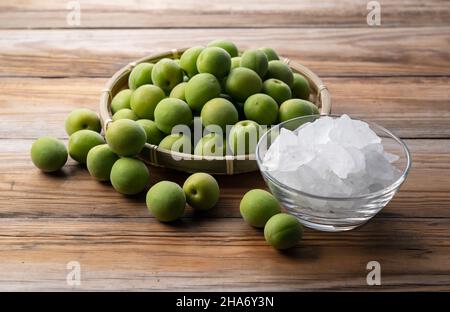 Unreife Ume-Frucht und Steinzucker auf einem hölzernen Hintergrund. Vorbereitung auf die Herstellung von japanischem Pflaumenwein Stockfoto