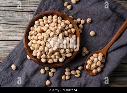 Getrocknete Kichererbsen in einer Holzschüssel vor einem alten Holzhintergrund, daneben ein Holzlöffel. Bild von Kichererbsen. Stockfoto