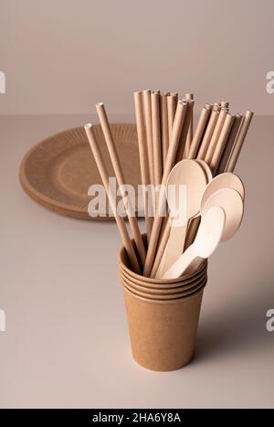 Braune Einweg-Pappbecher, Trinkhalme, Löffel und Teller auf beigefarbenem Hintergrund. Zero-Waste-Konzept. Stockfoto