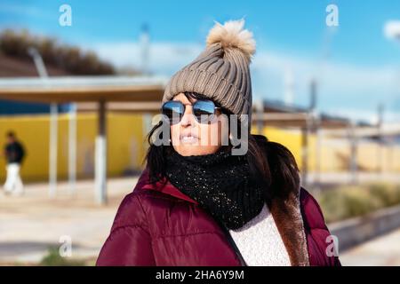 Porträt einer Frau mit Sonnenbrille und Wollmütze an einem sonnigen Herbsttag, der in der Stadt spazieren geht Stockfoto