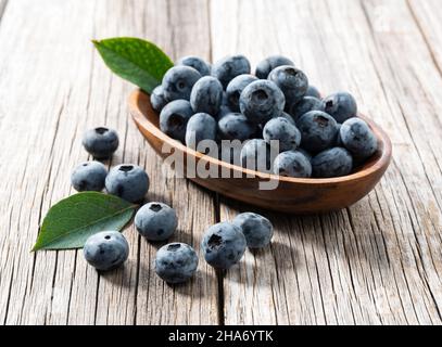 Brubery und Heidelbeerblätter auf einem alten Holzbrett. Blaubeeren in einer Holzschüssel dahinter. Stockfoto
