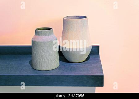 Elegant geformter Keramiktopf und Vase auf einem blauen Regal an einer cremefarbenen Wand für Einfachheit. Bild für künstlerische Zwecke eingefärbt. Stockfoto