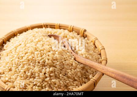 Brauner Reis in einem Bambuskolander und ein Holzlöffel auf einem hölzernen Hintergrund. Ein Haufen brauner Reis. Stockfoto