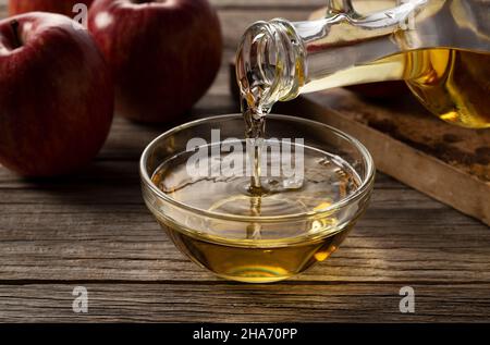 Sobald Sie Apfelessig in einen Glasbehälter vor einem hölzernen Hintergrund gießen. Stockfoto