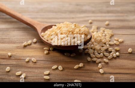 Brauner Reis in einem Holzlöffel auf einem hölzernen Hintergrund platziert. Ein Haufen brauner Reis. Stockfoto