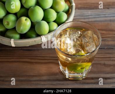 Japanischer Pflaumenwein und unreife Pflaumen auf einem Holzhintergrund. Stockfoto