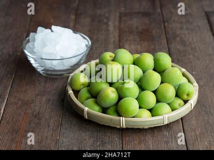 Unreife Ume-Frucht und Steinzucker auf einem hölzernen Hintergrund. Vorbereitung auf die Herstellung von japanischem Pflaumenwein Stockfoto