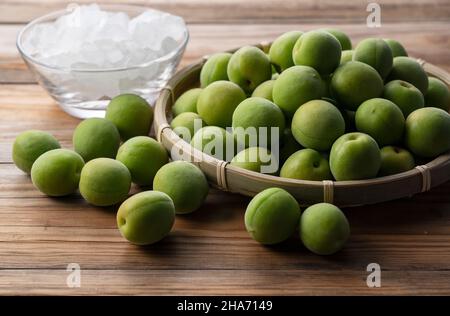 Unreife Ume-Frucht und Steinzucker auf einem hölzernen Hintergrund. Vorbereitung auf die Herstellung von japanischem Pflaumenwein Stockfoto