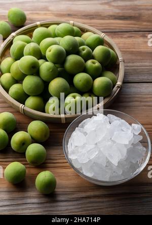 Unreife Ume-Frucht und Steinzucker auf einem hölzernen Hintergrund. Vorbereitung auf die Herstellung von japanischem Pflaumenwein Stockfoto