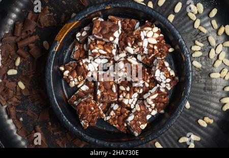 Schokoladenstücke mit aufgeblasenen Reis in einer schwarzen Schüssel auf einem dunklen Tisch mit Haselnusscreme Stockfoto