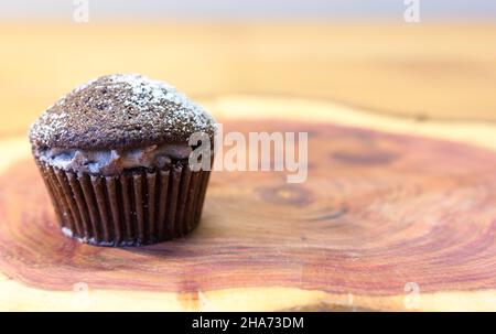 Schokoladen-Victoria-Sponge-Mini-Cup-Kuchen mit Kakaocreme gefüllt und mit Zucker auf Kirschholzplatte mit Platz für Text bestäubt Stockfoto