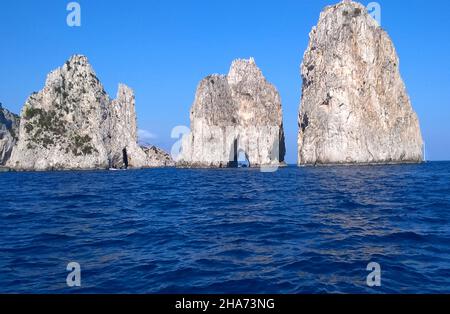 Die Felsformation Faraglioni de Mezzo, kurz vor der Insel Capri, Italien, gilt als die ikonischste Sehenswürdigkeit der Insel Es ist eine Tradition, dass das Küssen eines Partners unter dem kleinen Bogen, während ein Boot durch ihn fährt, dem betreffenden Paar Glück bringt. Stockfoto