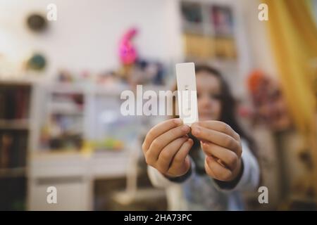 Details zur geringen Schärfentiefe (selektiver Fokus) mit den Händen eines 6-jährigen Mädchens, das einen COVID-19 Antigen Rapid Test hält, mit einem negativen Ergebnis. Stockfoto