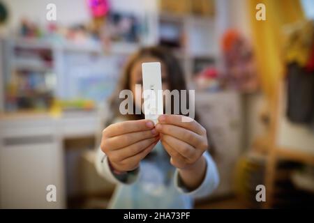 Details zur geringen Schärfentiefe (selektiver Fokus) mit den Händen eines 6-jährigen Mädchens, das einen COVID-19 Antigen Rapid Test hält, mit einem negativen Ergebnis. Stockfoto