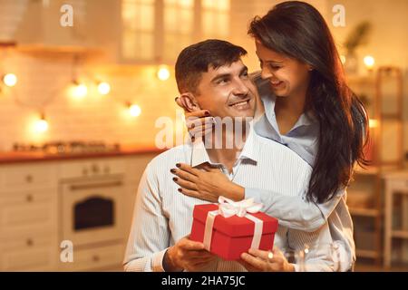 Freudig aufgeregt Mann erhielt ein Geschenk von seiner Freundin, die hinter ihm steht und umarmt ihn. Stockfoto