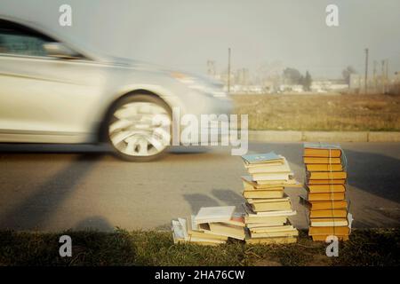 Ein Haufen alter Bücher, die auf dem Gras an der Straße liegen, weggeworfen. Stockfoto