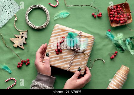 Umweltfreundliche Dekorationen - recyceltes Bastelpapier, Federn, Beeren, Wattkranz, Holz-Weihnachtsspielzeug. Hände Verpackung Weihnachten Geschenkbox mit Stockfoto