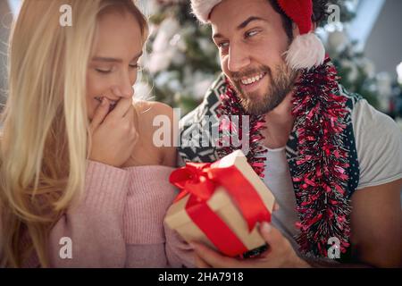 Festliches kaukasisches Paar, das an einem Weihnachtsmorgen Weihnachtsgeschenke austauscht; Feiertagsfreude-Konzept Stockfoto