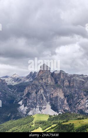 Schöne Aussicht auf den Berg Sassongher mit niedrigen Regenwolken und einer von der Sonne beleuchteten Wiese am Fuß Stockfoto