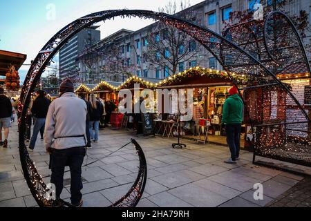Weihnachtslichter verleihen den kleinen Holzbuden auf dem Plymouth Christmas Market eine Wärme, Masken zeigen, dass Covid es ist. Stockfoto