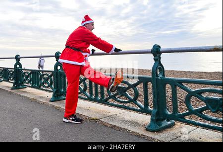 Brighton UK 11th December 2021 - Stretching before taking part in this years Brighton Santa Dash on Hove Seafront which hoves money for the Rockinghorse Charity : Credit Simon Dack / Alamy Live News Stockfoto