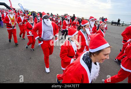 Brighton UK 11th December 2021 - Hunderte von Läufern nehmen in diesem Jahr an Brighton Santa Dash an der Küste von Hove Teil, das Geld für die Rockinghorse-Wohltätigkeitsorganisation sammelt : Credit Simon Dack / Alamy Live News Stockfoto