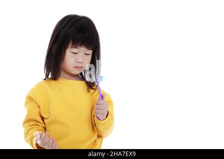 Schlampiges asiatisches Kind im Schlafanzug mit Zahnbürste, Mundgesundheitskonzept. Isoliert auf weißem Hintergrund. Nettes chinesisches Mädchen, das früh am Morgen aufwacht Stockfoto