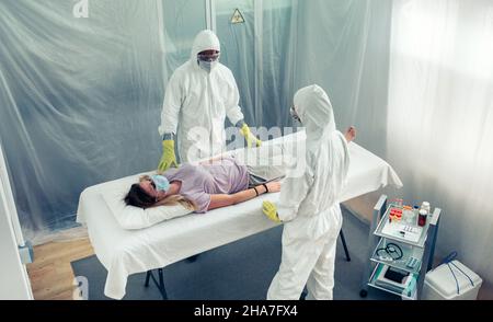 Ärzte in einem bakteriologischen Schutzanzug beobachten einen Patienten, der auf einer Liege in einem Feldkrankenhaus liegt Stockfoto