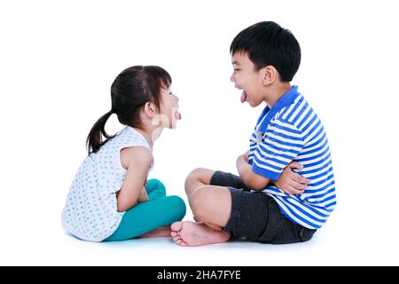 Schlechtes Verhalten. Ganzer Körper asiatischer Kinder ragen aus Zungen und spotten sich gegenseitig. Schwester und Bruder sitzen im Studio, isoliert auf weißem Backgro Stockfoto