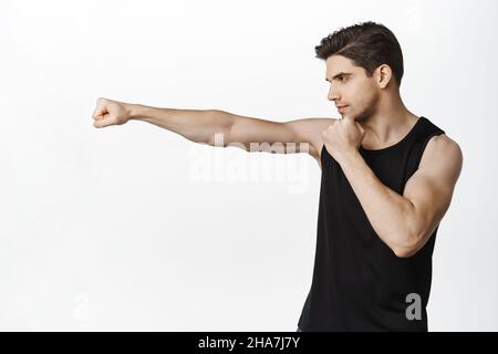 Bild eines gutaussehenden starken männlichen Athleten, eines Sportlers, der eine geballte Faust ausstreckt, im Fitnessstudio trainiert, kämpft, auf weißem Hintergrund steht Stockfoto