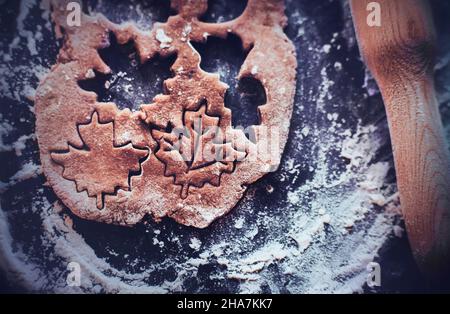 Auf einem Backblech, das mit Mehl bestreut ist, befindet sich ein hölzerner Nudelholz und ein Teig, aus dem Lebkuchenfiguren ausgeschnitten werden. Hausgemachte Kuchen für CH Stockfoto