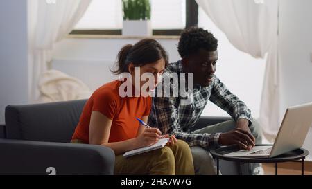 Interracial paar tun Steuern Zahlung mit Laptop im Wohnzimmer. Junge gemischte Rennpartner berechnen Geld und Budget für die Finanzplanung und zahlen Rechnungen auf der Couch zu Hause Stockfoto