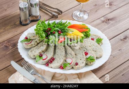 Fischgericht: Fischfilet mit Gemüse und Kräutern auf einem weißen Teller auf dunklem Holzboden Stockfoto