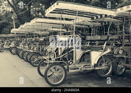 Reihe von Vintage-Pedal-Power vierrädrigen surrey Fahrrad zur Miete auf dem Parkplatz im öffentlichen Park. Verleih von Retro-Quad-Bikes in Sepia getönten. Stockfoto