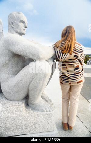 1980S RÜCKANSICHT EINER ANONYMEN BLONDEN FRAU, DIE NEBEN EINER MÄNNLICHEN SKULPTUR VON GUSTAV VIGELAND IM FROGNER PARK OSLO NORWEGEN STEHT - 013390 AND001 HARS IN VOLLER LÄNGE DAMEN PERSONEN INSPIRATION MÄNNER NÄCHSTE SKULPTUR ERHOLUNG RÜCKANSICHT EIN IN DER KONZEPTIONELLEN VON HINTEN NEBEN STILVOLLEN ANONYMEN RÜCKANSICHT ENTSPANNUNG STATUEN ZWEISAMKEIT JUNGE ERWACHSENE FRAU KAUKASISCHE ETHNIE GRANIT GUSTAV INSTALLATION WAHRZEICHEN NORWEGEN ALTMODISCH Stockfoto