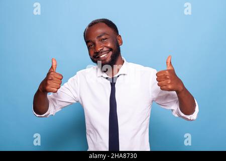 Portratit des lächelnden optimistischen Geschäftsmannes, der den Geschäftserfolg mit zwei Daumen hochjubelte. Fröhliche Person tut Handgesten für große Leistung. Stockfoto