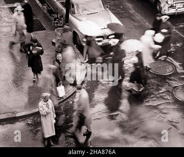 1950S ÜBERFÜLLTE STRASSENFUSSGÄNGER UND VERKEHR IM REGENSTURM - C1279 CLE003 HARS MÄNNER REGENSCHIRME REGNENDE FUSSGÄNGER STÜRMISCHER TRANSPORT S/W HOCHWINKEL KREUZUNGSSCHUTZ STRASSEN UND AUTOS ASPHALT BEWEGUNG UNSCHÄRFE AUTOS FAHRZEUGE REGENMÄNTEL SCHLECHTES WETTER SCHWARZ UND WEISS ALTMODISCH Stockfoto