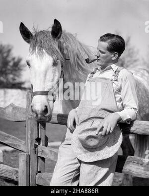 1920S BAUER RAUCHT PFEIFE TRAGEN OVERALLS AUF HOLZZAUN LEHNEND MIT STROH HAT BLICK AUF SEINE DAPFEL GRAU ZUGARBEIT PFERD - H2683 HAR001 HARS HOME LEBEN KOPIEREN RAUM FREUNDSCHAFT HALBLANGE PERSONEN OVERALLS FÜRSORGLICH LANDWIRTSCHAFT MÄNNER VERTRAUEN LANDWIRTSCHAFT B&W RUHE SEINE STÄRKE BAUERN KRAFTVOLLEN STOLZ AUF ZUFRIEDENHEIT BERUFE SPLIT RAIL KONZEPTIONELLE LIEBLINGS KONTEMPLATION ENTWURF ZUSAMMENARBEIT GRAUES SÄUGETIER MITTLEREN ERWACHSENEN MITTLEREN ERWACHSENEN MANN ENTSPANNUNG SCHWARZ-WEISS KAUKASISCHE ETHNIZITÄT HAR001 ALTMODISCH Stockfoto